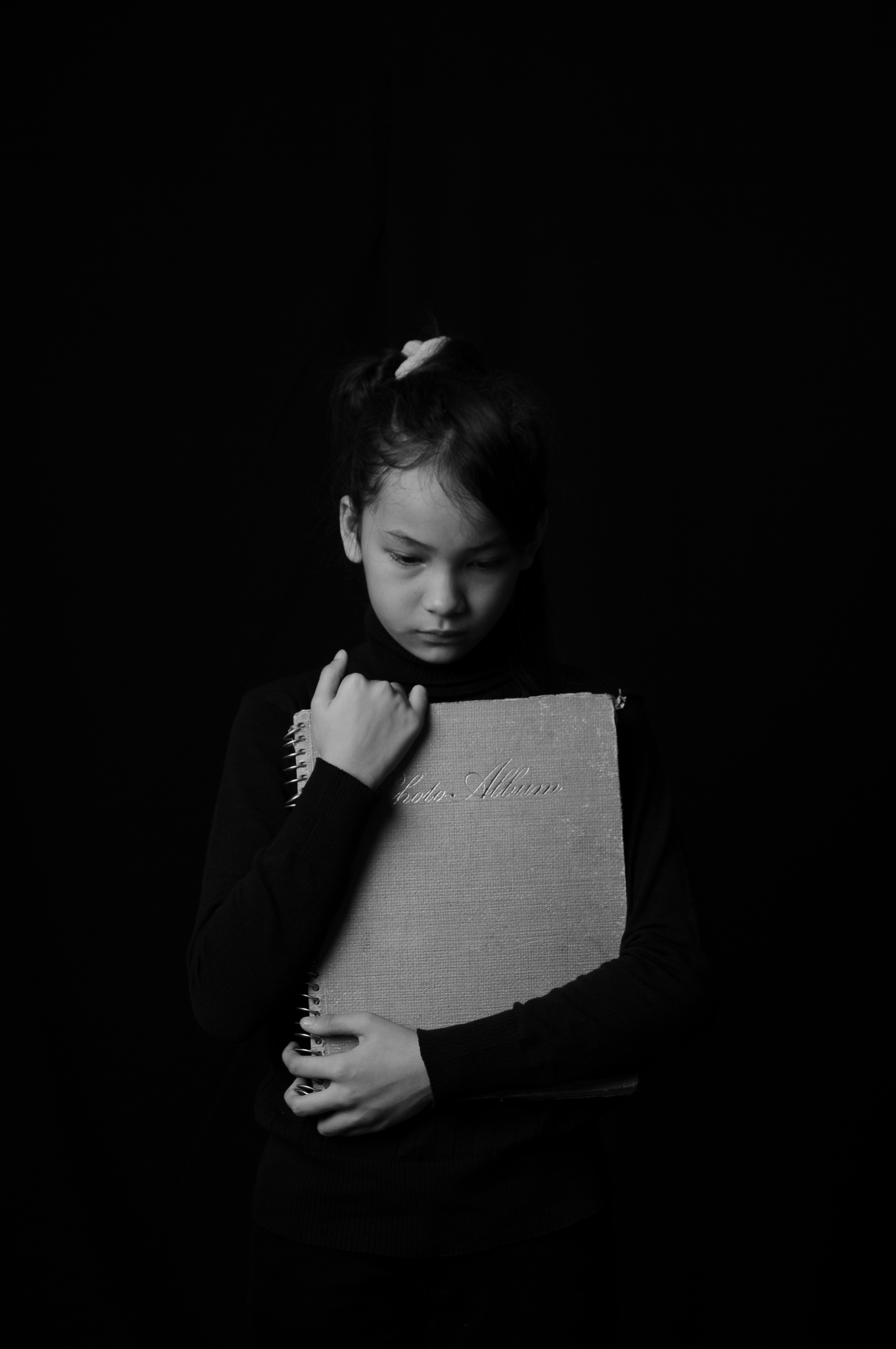 A young girl hugging a book against her body in a black and white photo